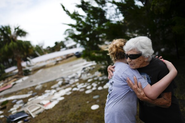 FILE - Tina Brotherton, 88, gets a hug from 9-year-old neighbor Lainey Hamelink, as she returns to site of her business, Tina's Dockside Inn, which was completely destroyed in Hurricane Idalia, as was Brotherton's nearby home, in Horseshoe Beach, Fla., Friday, Sept. 1, 2023, two days after the storm's passage. A resident of Horseshoe Beach since 1978, she lost her marina and the cafe next door in a 1993 disaster and had to replace the floors and beds at Tina's Dockside Inn. Now the hotel, which she has owned for 52 years, is destroyed in Idalia's wake. (AP Photo/Rebecca Blackwell, File)