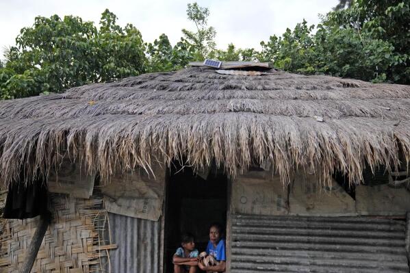 Imelda Pindi Mbitu, right, sits next to one of her of five children at the entrance of her house as a solar panel is seen on its roof in Walatungga on Sumba Island, Indonesia, Tuesday, March 21, 2023. For years she would have to manually pound the kernels and beans between two rocks for hours at a time, now she uses a solar-powered machine. (AP Photo/Dita Alangkara)