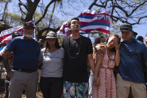Community organizer Tiare Lawrence, second from right, is comforted by Archie Kalepa as they sing a song during a news conference with Lahaina, Hawaii, residents affected by a deadly wildfire in Lahaina, Hawaii, Friday, Aug. 18, 2023. (AP Photo/Jae C. Hong)