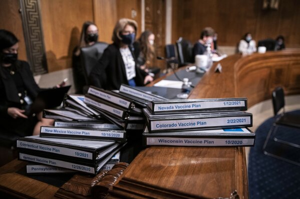 Folders detailing the COVID vaccine plans for states are stacked on a table during a confirmation hearing for Secretary of Health and Human Services nominee Xavier Becerra before the Senate Health, Education, Labor and Pensions Committee, Tuesday, Feb. 23, 2021 on Capitol Hill in Washington. (Sarah Silbiger/Pool via AP)