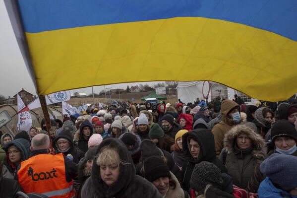 FILE - A Ukrainian volunteer Oleksandr Osetynskyi, 44 holds a Ukrainian flag and directs hundreds of refugees after fleeing from the Ukraine and arriving at the border crossing in Medyka, Poland, Monday, March 7, 2022. War has been a catastrophe for Ukraine and a crisis for the globe. One year on, thousands of civilians are dead, and countless buildings have been destroyed. Hundreds of thousands of troops have been killed or wounded on each side. Beyond Ukraine’s borders, the invasion shattered European security, redrew nations’ relations with one another and frayed a tightly woven global economy. (AP Photo/Visar Kryeziu, File)