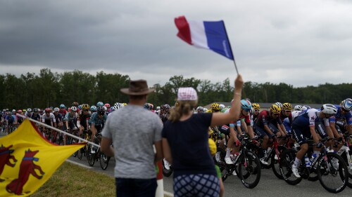 FILE - Spectators wave flags as the pack rides during the nineteenth stage of the Tour de France cycling race over 188.5 kilometers (117.3 miles) with start in Castelnau-Magnoac and finish in Cahors, France, Friday, July 22, 2022. The 110th edition of the Tour de France starting Saturday, July 1, 2023, from Bilbao, Spain. (AP Photo/Thibault Camus, File)