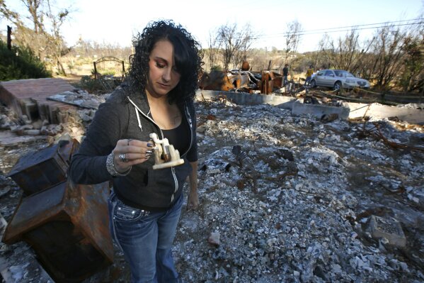 In this Friday, Oct. 18, 2019, photo, Amber Blood looks at a figurine she found in the ashes of her home lost in last year's Camp Fire in Paradise, Calif. Blood is one of the estimated 20,000 former Paradise residents now living in Chico after the fire. A real estate agent, Blood said she even had trouble finding a home after the fire because there was not much available. (AP Photo/Rich Pedroncelli)