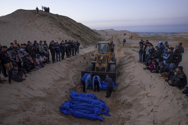 A bulldozer unloads the bodies of Palestinians killed in fighting with Israel and turned over by the Israeli military during a mass funeral in Rafah, Gaza Strip, Tuesday, Dec. 26, 2023.(AP Photo/Fatima Shbair)