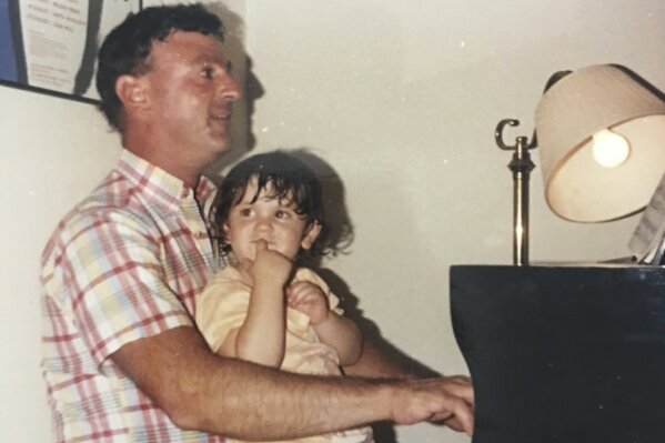 This undated photo provided by the family in May 2020 shows Joseph Policelli at the piano with his niece Stephanie Mayne. At funerals, he made the organ moan, and at weddings, it thundered in joy. On Christmas, bells twinkled; on Easter, trumpets blasted. He delivered victorious graduation marches and bellowing birthday celebrations, blaring the pipes and vibrating the pews every Sunday in between. He was unassuming, egoless and largely anonymous, but in the lives of generations of Catholics in communities around Massachusetts, Policelli played the soundtrack. He died from COVID-19 on April 27, 2020 at 71. (Family photo via AP)