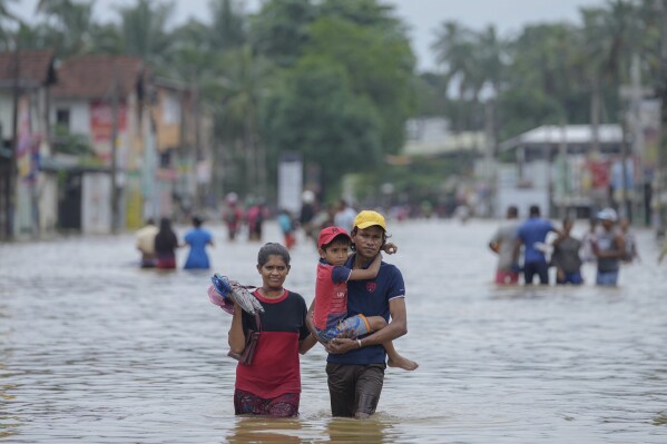 People wade through a flooded street in Biyagama, a suburb of Colombo, Sri Lanka, Monday, Jun. 3, 2023. Sri Lanka closed schools on Monday as heavy rains triggered floods and mudslides in many parts of the island nation, killing at least 10 people while six others have gone missing, officials said. (AP Photo/Eranga Jayawardena)