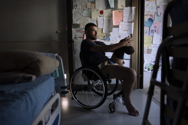 Israeli soldier Jonathan Ben Hamou, 22, wounded in the war with Hamas, sits in his room at Sheba hospital's rehabilitation division, in Ramat Gan, Israel, Monday, Dec. 18, 2023. Ben Hamou was wounded in the Gaza Strip when a rocket-propelled grenade struck the bulldozer he was using to help clear the way for other troops and dig trenches. He lost his left leg beneath the knee. (AP Photo/Oded Balilty)