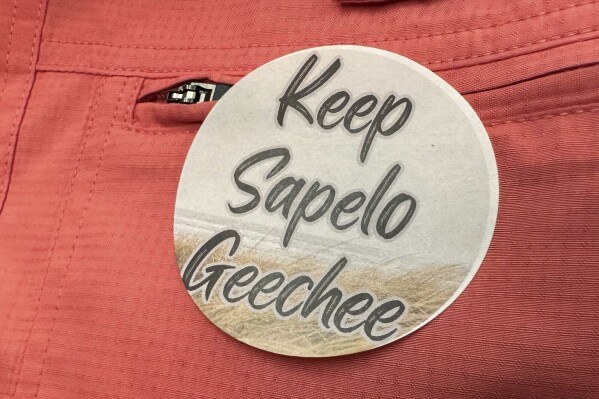 A sticker saying "Keep Sapelo Geechee" is worn on the shirt of George Grovner, a resident of the Hogg Hummock community on Sapelo Island, during a meeting of McIntosh County commissioners Tuesday, Sept. 12, 2023, in Darien, Ga. Commissioners voted to double the maximum size of homes allowed in the tiny community of people known as Gullah-Geechee, who are descended from slaves who worked coastal plantations. Residents say they fear the zoning change will raise their property values and taxes, potentially forcing them to sell their land. (AP Photo/Ross Bynum)