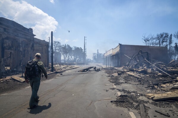 In this photo provided by Tiffany Kidder Winn, a man walks past wildfire wreckage on Wednesday, Aug. 9, 2023, in Lahaina, Hawaii. The scene at one of Maui's tourist hubs on Thursday looked like a wasteland, with homes and entire blocks reduced to ashes as firefighters as firefighters battled the deadliest blaze in the U.S. in recent years. (Tiffany Kidder Winn via AP)