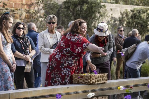 Gaye Myler, center, throws a flower into a reflection pool at Port Arthur, Australia, Wednesday, April 28, 2021, as Australia marks the 25th anniversary of a lone gunman killing 35 people in Tasmania state in a massacre that galvanized the nation into tightening gun laws. (Luke Bowden/Pool via AP)