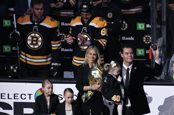 Former Boston Bruins goalie Tuukka Rask, right, holds up a puck during ceremony honoring his retirement, before the team's NHL hockey game against the New Jersey Devils, Thursday, March 31, 2022, in Boston. With Rask is wife, Jasmiina, and three daughters, Vivien, Adelie, and Livia, from left. (AP Photo/Charles Krupa)