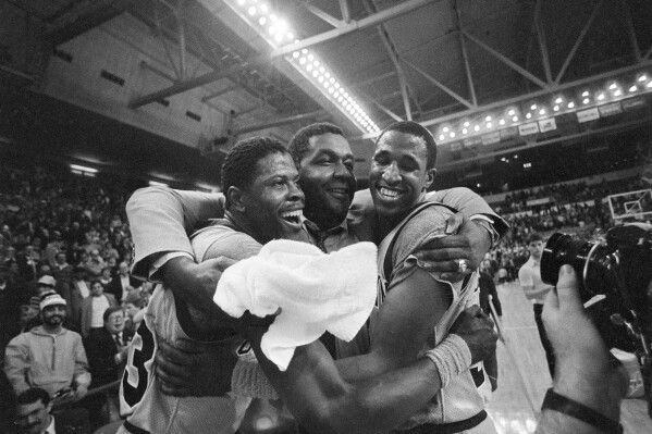 FILE - Georgetown University's Patrick Ewing, left, and teammate Ralph Dalton, right, get a hug from head coach John Thompson, center, after Georgetown downed Georgia Tech 60-54 during NCAA an NCAA college basketball game in Providence, R.I., March 24, 1985. (AP Photo/Paul Benoit, File)