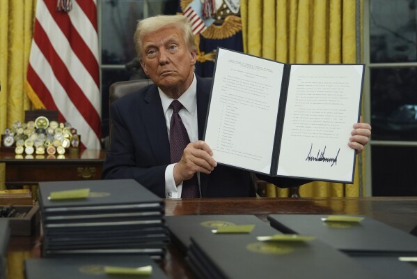 President Donald Trump holds up an executive order commuting sentences for people convicted of Jan. 6 offenses in the Oval Office of the White House, Monday, Jan. 20, 2025, in Washington. (AP Photo/Evan Vucci)