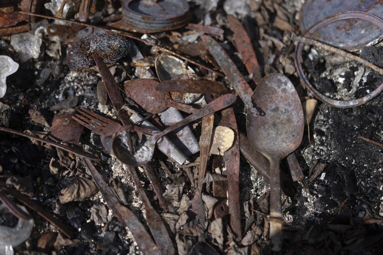 Burnt spoons, forks and knives lie on the ground among the remains of Julia Cardinal's cabin that was destroyed by wildfires, near Fort Chipewyan, Canada, on Sunday, Sep. 3, 2023. (AP Photo/Victor R. Caivano)