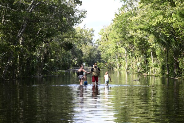 Dustin Holmes, second from right, holds hands with his girlfriend, Hailey Morgan, while returning to their flooded home with her children Aria Skye Hall, 7, right, and Kyle Ross, 4, in the aftermath of Hurricane Helene, Sept. 27, 2024, in Crystal River, Fla. (AP Photo/Phelan M. Ebenhack, File)