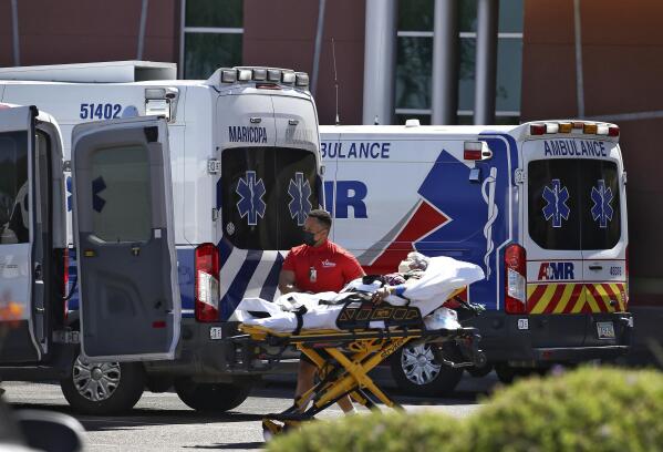 FILE - A person is brought to a medical transport vehicle from Banner Desert Medical Center as several transports and ambulances are shown parked outside the emergency room entrance in Mesa, Ariz., on June 16, 2020. Arizona reported 6,043 additional confirmed COVID-19 cases and 174 virus deaths Saturday, Dec. 4, 2021, as the pandemic's latest surge maintained its grip on the state. (AP Photo/Ross D. Franklin, File)