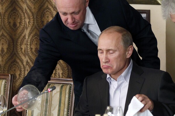 FILE - Yevgeny Prigozhin, top, serves food to then-Russian Prime Minister Vladimir Putin at Prigozhin's restaurant outside Moscow, Russia, on Nov. 11, 2011. Prigozhin made his name as the profane and brutal mercenary boss who mounted an armed rebellion that was the most severe and shocking challenge to Russian President Vladimir Putin’s rule. (AP Photo/File)