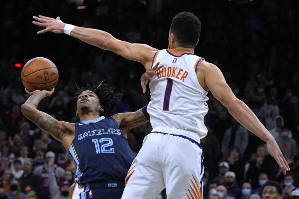 Memphis Grizzlies guard Ja Morant scores against Phoenix Suns guard Devin Booker (1) in the last second of an NBA basketball game Monday, Dec. 27, 2021, in Phoenix. The Grizzlies won 114-113. (AP Photo/Rick Scuteri)