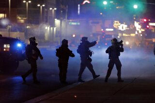 FILE - In this May 30, 2020, file photo, police walk through tear gas as they try to disperse protesters in Las Vegas. Three Nevada men with ties to a loose movement of right-wing extremists advocating the overthrow of the U.S. government have been arrested on terror charges in what authorities say was a conspiracy to spark violence during recent protests in Las Vegas. (AP Photo/John Locher, File)