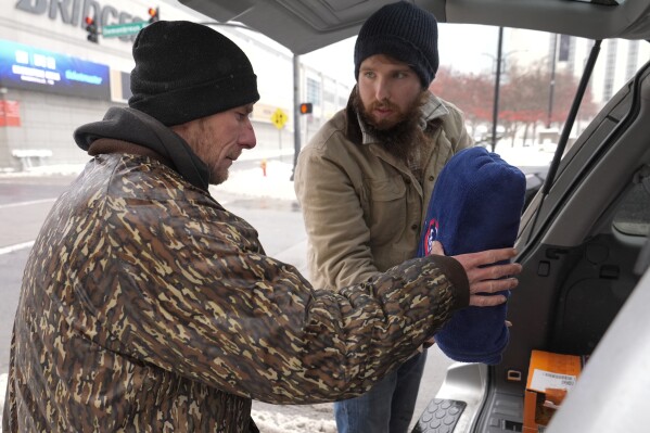 Will Compton, right, gives Luke Hall a blanket Thursday, Jan. 18, 2024, in Nashville, Tenn. Compton a resource specialist for the homeless outreach organization Open Table Nashville, has been canvassing the area helping the homeless during a recent winter storm. (AP Photo/George Walker IV)