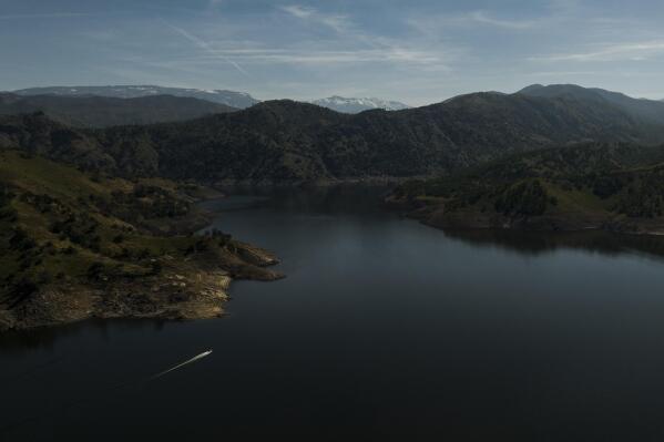 A boat crosses Pine Flat Lake as snow-capped mountains are visible in the distance in the Sierra National Forest, Calif., Friday, April 21, 2023. The reservoir can hold up to 1 million acre feet of water and is expected to receive more than 3 million acre feet this spring from the melting snow, according to David Merritt, general manager for the Kings River Conservation District. (AP Photo/Jae C. Hong)