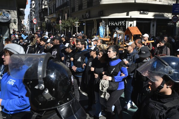 Police walk alongside people marching from San Cayetano church to downtown Buenos Aires, Argentina, to keep protesters from blocking the street, Wednesday, Aug. 7, 2024, on the feast day of St. Cajetan, known as the patron of the unemployed. Others joined their march to protest for work opportunities. (AP Photo/Gustavo Garello)