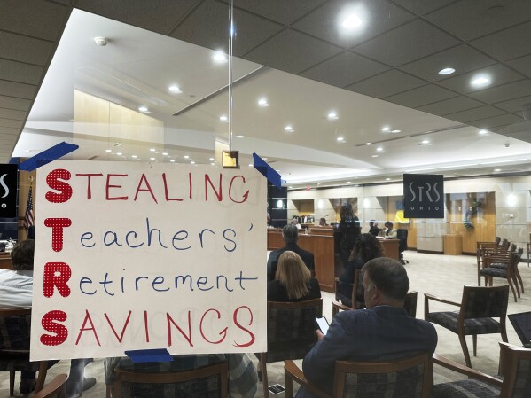 A poster using the initials of the State Teachers Retirement System of Ohio to spell out "Stealing Teachers' Retirement Savings" hangs on the wall during a board meeting at the pension fund's headquarters in Columbus, Ohio, on Wednesday, May 15, 2024. (AP Photo/Julie Carr Smyth)
