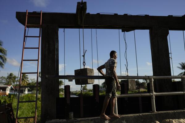 Gate operator Hakim Altaf checks the gate on the seawall in Georgetown, Guyana, Thursday, April 13, 2023. The seawall relies on dozens of workers like Altaf, who set alarms night and day to manually open and close sluice gates known as “kokers” that prevent the Atlantic Ocean from flooding Guyana. (AP Photo/Matias Delacroix)