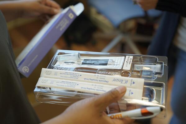 Kristin Travis, a community outreach doula, holds a home COVID-19 test kit Thursday, Feb. 3, 2022, while picking up supplies at Open Arms Perinatal Services before going out to visit some of her clients in Seattle. With the brutal omicron wave rapidly easing its grip, new cases of COVID-19 in the U.S. are falling in 49 of the 50 states. (AP Photo/Ted S. Warren)