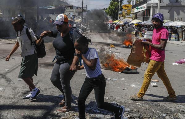 People walk past tires set fire as part of an anti-government protest in Port-au-Prince, Haiti, Thursday, Oct. 21, 2021. Demonstrators decry a severe fuel shortage and a spike in insecurity as they demanded that Prime Minister Ariel Henry step down. (AP Photo/Odelyn Joseph)