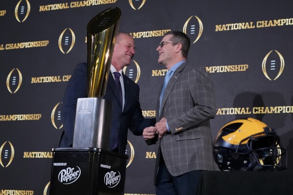 Washington head coach Kalen DeBoer, left, and Michigan head coach Jim Harbaugh shake hands near the trophy after a news conference ahead of the national championship NCAA College Football Playoff game between Washington and Michigan Sunday, Jan. 7, 2024, in Houston. The game will be played Monday. (AP Photo/Godofredo A. Vasquez)