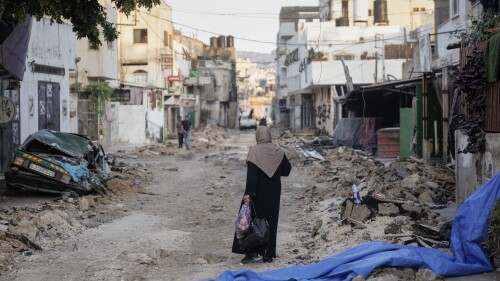 A Palestinian woman walks on a damaged road in the Jenin refugee camp in the West Bank, Wednesday, July 5, 2023, after the Israeli army withdrew its forces from the militant stronghold. The withdrawal of troops from the camp ended an intense two-day operation that killed at least 13 Palestinians, drove thousands of people from their homes and left a wide swath of damage in its wake. One Israeli soldier was also killed. (AP Photo/Majdi Mohammed)