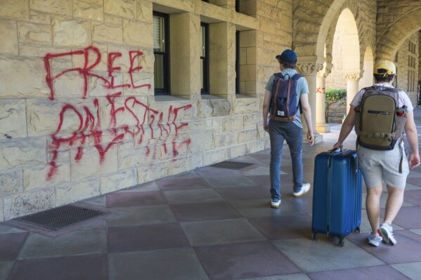 Students walk by graffiti near university president Richard Saller's office at Stanford University in Palo Alto, Calif., Wednesday, June 5, 2024. Stanford University said 13 people were arrested as law enforcement removed pro-Palestinian demonstrators who occupied a campus building early Wednesday that houses the university president and provost offices, with the school saying there was extensive damage inside and outside the building and an officer was lightly injured. (AP Photo/Nic Coury)