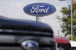 FILE - In this Sunday, Oct. 11, 2020, file photo, the company logo hangs over a row of 2020 F-150 pickup trucks at a Ford dealership, in Denver. A global semiconductor shortage and a February 2021 winter storm have combined to force Ford to build F-150 pickup trucks without some computers. The company says the pickups will be held at factories for “a number of weeks,” then shipped to dealers once computers are available and quality checks are done. (AP Photo/David Zalubowski, File)