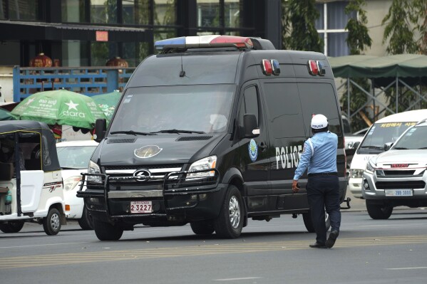FILE - A Cambodian police man directs traffic as a convoy of police vehicles that was reportedly carrying Japanese citizens who were taken into custody on suspicion of running phone scams moves along a street on their way to Phnom Penh International Airport in Phnom Penh, Cambodia, on April 11, 2023. Twenty-five Japanese nationals suspected of involvement in an online scam operation based in Cambodia were deported to Japan on Wednesday, Nov. 8, said Gen. Khieu Sopheak, a spokesperson for Cambodia's Interior Ministry. (AP Photo/Heng Sinith, File)