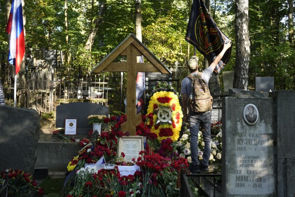 A man straightens a flag of the Wagner private military contractor at the grave of Yevgeny Prigozhin at Porokhovskoye Cemetery in St. Petersburg, Russia, on Friday, Sept. 22, 2023. Prigozhin, the head of Wagner, was killed on Aug. 23 when a private jet carrying him and his top lieutenants crashed while flying from Moscow to St. Petersburg, killing all 10 people aboard. (AP Photo/Dmitri Lovetsky)
