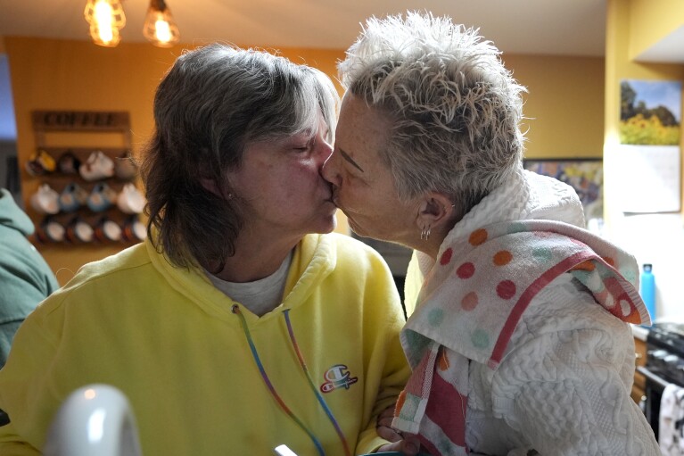 Deb Robertson, right, kisses her wife of over 40 years, Kate Koubek as they prepare for a BBQ with family and friends at their Lombard, Ill., home Saturday, March 23, 2024, in Lombard, Ill. Robertson didn’t cry when she learned two months ago that the cancerous tumors in her liver were spreading, portending a tormented death. But later, she cried after receiving a call that a bill moving through the Illinois Legislature to allow certain terminally ill patients to end their own lives with a doctor’s help had made progress. (AP Photo/Charles Rex Arbogast)