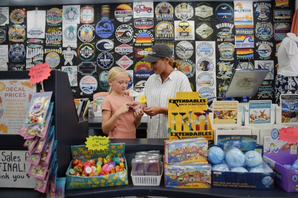 Michelle Rutkowski, owner of Boardwalk Best and Five Mile Marketplace, shows her daughter Harriet, 9, a toy at her shop in Wildwood, N.J., Friday, Aug. 9, 2024. (AP Photo/Matt Rourke)