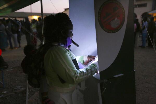 A woman uses her mobile phone to light the ballot box as she casts her vote at a polling station in Lusaka, Zambia, Thursday Aug, 12, 2021.  Zambias standing as one of Africa's most stable democracies is being tested as the country votes amid violence, alleged intimidation and fears of vote rigging. (AP Photo/Tsvangirayi Mukwazhi)