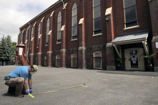 A worker marks socially distanced spots in a parking lot for parishioners, due to the coronavirus outbreak, outside St. Rose of Lima Catholic Church in Chelsea, Mass., Friday, May 29, 2020. Masses, which were stopped in March due to fears of spreading the coronavirus, will resume this weekend. (AP Photo/Charles Krupa)