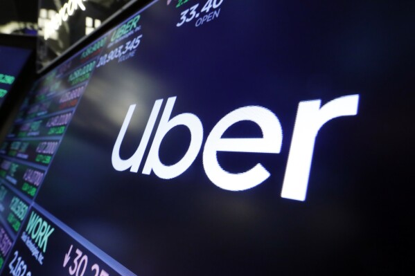 FILE - The logo for Uber appears above a trading post on the floor of the New York Stock Exchange, Aug. 16, 2019. Uber is shutting down alcohol delivery app Drizly, the company confirmed this week, just under three years after acquiring the platform for $1.1 billion. Drizly will officially shut down at the end of March, Uber told The Associated Press. (AP Photo/Richard Drew, File)