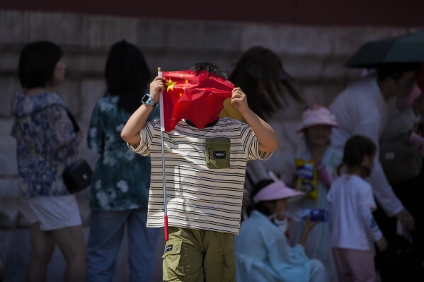 A boy uses a national flag to shield from the sun as visitors line up to enter the Forbidden City on a sweltering day in Beijing, Friday, July 7, 2023. (AP Photo/Andy Wong)
