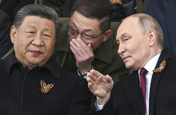 Russian President Vladimir Putin, right, and Chinese President Xi Jinping, left, talk as they watch the Victory Day military parade in Moscow, Russia, Friday, May 9, 2025, during celebrations of the 80th anniversary of the Soviet Union's victory over Nazi Germany during the World War II. (Sergei Bobylev/Photo host agency RIA Novosti via AP)