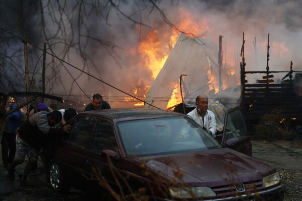 Residents push a car away from an encroaching forest fire in Villa Alemana, Valparaiso, Chile, Friday, Feb. 2, 2024. (Andres Pina, Aton Chile via AP)