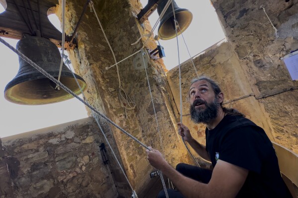 Sitting in a chair with ropes looped around both feet and hands, Joan Carles Osuna, a student of the Vall d'en Bas School of Bell Ringers, performs playing all four bronze bells at the church bell tower of the12th-century Sant Romà church, at the village of Joanetes, about two hours north of Barcelona, Spain, Saturday, June 29, 2024. A school set up to revive the manual ringing of church bells has graduated its first class of 18 students after learning their ringing skills. (AP Photo/Emilio Morenatti)