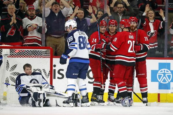Carolina Hurricanes' Seth Jarvis (24) celebrates his goal with teammates Teuvo Teravainen (86), Sebastian Aho (20) and Ian Cole (28) as Winnipeg Jets' Nate Schmidt (88) stands near Jets goaltender Eric Comrie (1) during the third period of an NHL hockey game in Raleigh, N.C., Thursday, April 21, 2022. (AP Photo/Karl B DeBlaker)