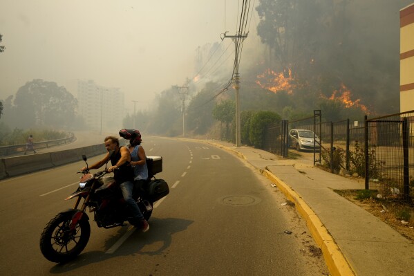 Obyvatelé se evakuují na motocyklu, zatímco kouř z lesních požárů zaplňuje oblohu a plameny se šíří ve Vina del Mar, Chile, v sobotu 3. února 2024. Úředníci říkají, že intenzivní lesní požáry kolem hustě obydlené oblasti ve středním Chile si vyžádaly několik mrtvých a zničily stovky lidí. domů..  (AP Photo/Esteban Felix)