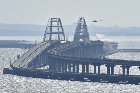 FILE - A helicopter drops water to stop fire on Crimean Bridge connecting Russian mainland and Crimean peninsula over the Kerch Strait, in Kerch, on Oct. 8, 2022. Traffic on the key bridge connecting Crimea to Russia’s mainland has been halted amid reports of explosions. The governor of Crimea, which was annexed by Russia in 2014, announced the closure early Monday, July 17, 2023, but did not specify the reason.(AP Photo, File)