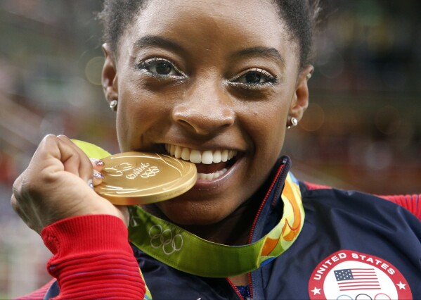 FILE - United States' Simone Biles bites her gold medal for the artistic gymnastics women's individual all-around final at the 2016 Summer Olympics in Rio de Janeiro, Brazil, Aug. 11, 2016. USA Gymnastics announced Wednesday, June 28, 2023, that Biles, the 2016 Olympic champion, will be part of the field at the U.S. Classic outside of Chicago on Aug. 5. The meet will be Biles' first since the 2020 Olympics. (AP Photo/Dmitri Lovetsky)