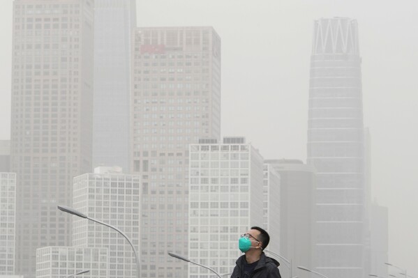 A man wearing a face mask walks on an overhead bridge against the office buildings in the central business district as dust and sand storm sweeps through Beijing, Thursday, April 13, 2023. (AP Photo/Andy Wong)